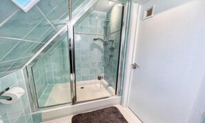 Un área de ducha con paredes de vidrio, una bañera blanca, paredes con azulejos y una puerta.