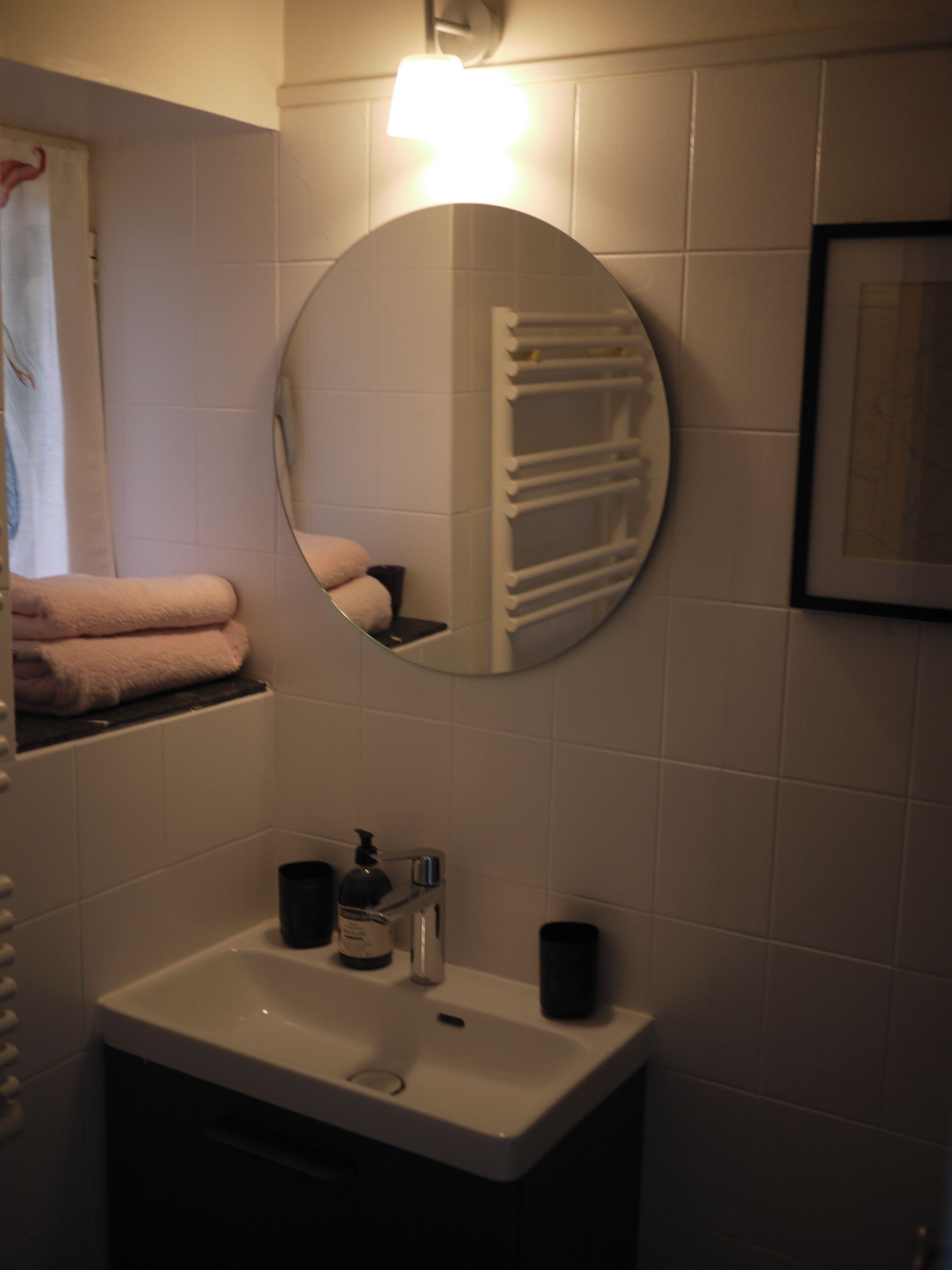 Een badkamer met een wit wastafelmeubel, een spiegel, een handdoekhouder en een ingelijst schilderij aan de muur.