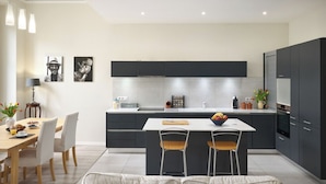 A modern kitchen with a central island, dark cabinets, and a dining area with a table and chairs. - Sunlight Properties GISELE: Hyper centre, 1 bedroom with bright modern living (Nice)