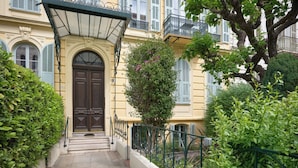 A narrow, stone-paved pathway leading to a building with a dark wooden door, flanked by lush greenery and a metal railing. - Sunlight Properties GISELE: Hyper centre, 1 bedroom with bright modern living (Nice)