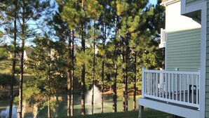 A residential area with a pond, tall pine trees, and a white fence.