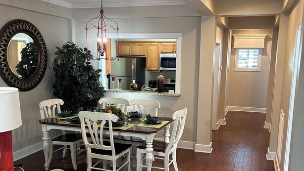 A dining area with a wooden table and white chairs, a large mirror, and a potted plant.