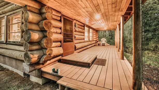 A log cabin with a wooden deck, large windows, and a porch extending into a forested area. - 76gs - Genuine Log Cabin - Wifi - Pets Ok - Sleeps 4 (Deming)