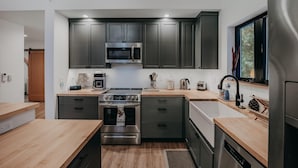 Une cuisine moderne avec des meubles de couleur sombre, des appareils en acier inoxydable et des plans de travail en bois.