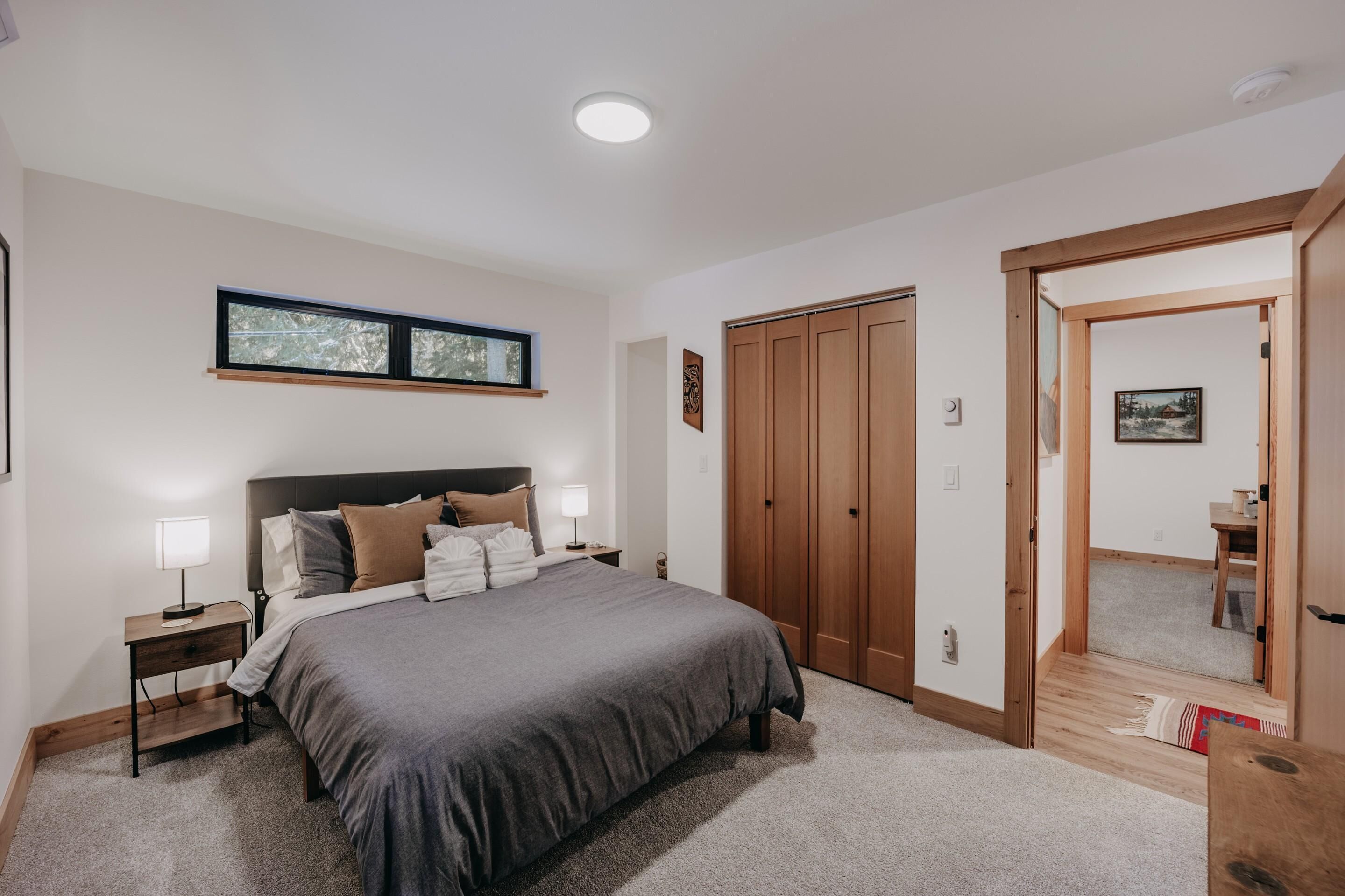 Quarto com uma cama grande, guarda-roupa de madeira e janela com vista para árvores.