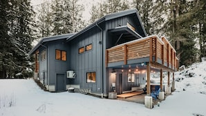Une maison moderne à deux étages, dotée d’un porche abrité et surplombant un paysage enneigé.
