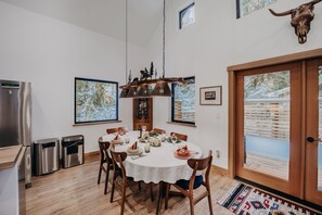 A dining area with a round table set for four, wooden chairs, a chandelier, and a mounted animal skull on the wall. - Mt Baker Rim Cabin 50 With Wifi, Hot Tub and Air Conditioning (Deming)