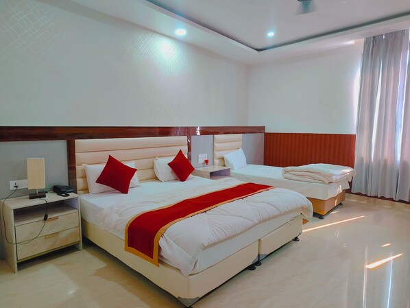A hotel room with two beds, a nightstand with a lamp and phone, and a large window with curtains. - Sitaynam Hotel & Resort-Infront RAM Temp (Ayodhya)