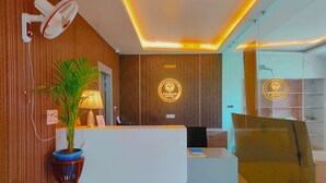 Zona de recepción de un hotel con diseño moderno, que incluye un mostrador, una planta en maceta e iluminación empotrada en el techo.