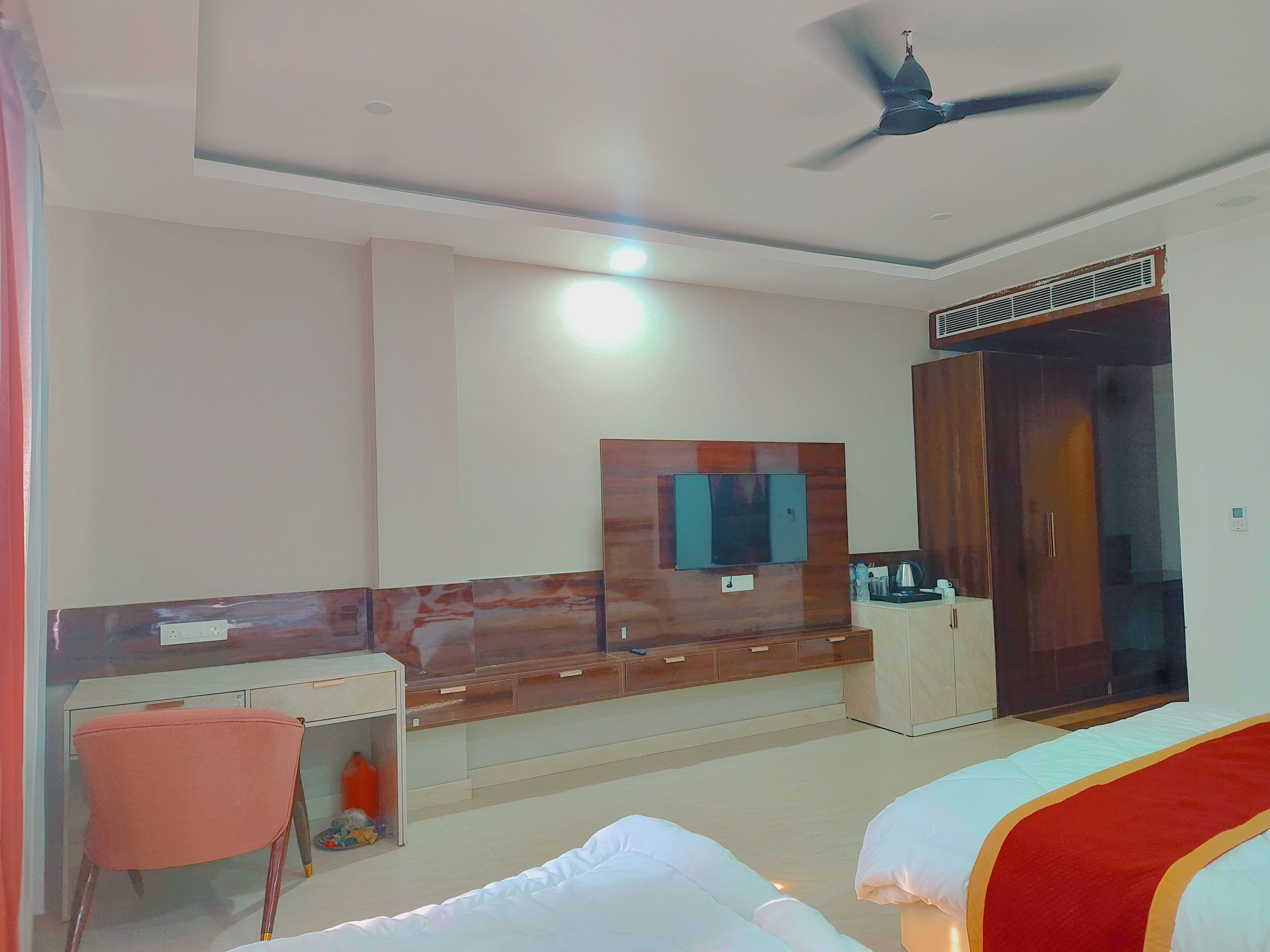 A hotel room with a bed, a desk, a chair, a wardrobe, a television, and a ceiling fan.