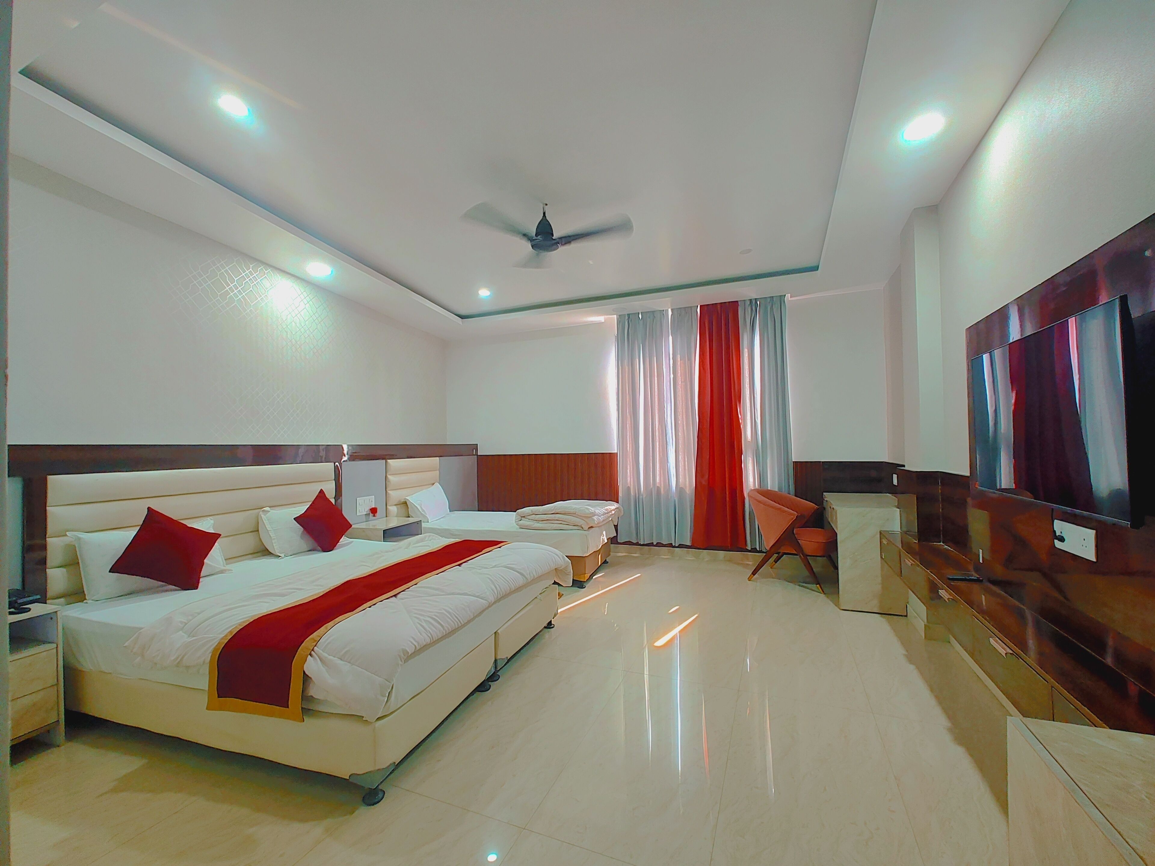 A hotel room with two beds, a TV, a ceiling fan, and a large window with curtains.