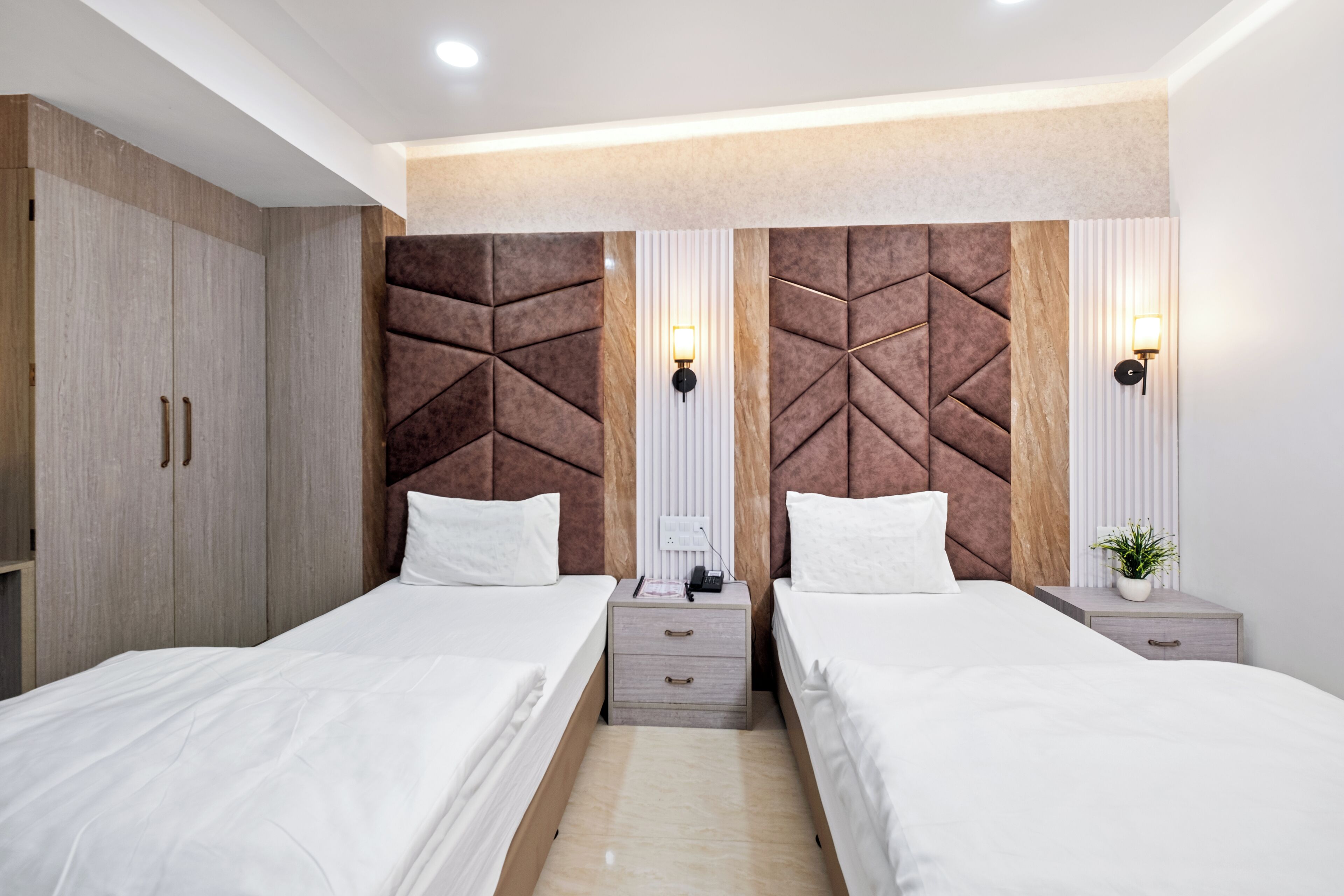 Une chambre moderne avec deux lits, des têtes de lit en bois, des tables de chevet et des lampes fixées au mur.