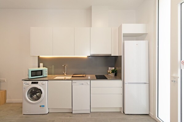 A compact kitchen with a washing machine, microwave, dishwasher, and refrigerator.