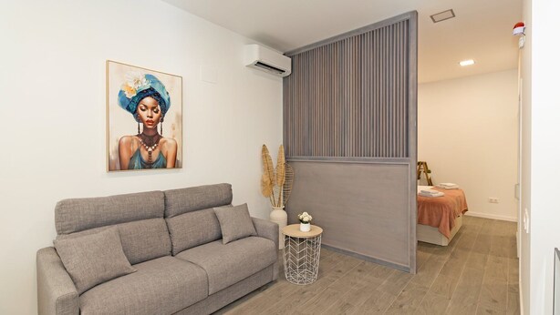 Ein modernes Wohnzimmer mit einem grauen Sofa, einem kleinen runden Beistelltisch und einem Gemälde an der Wand.