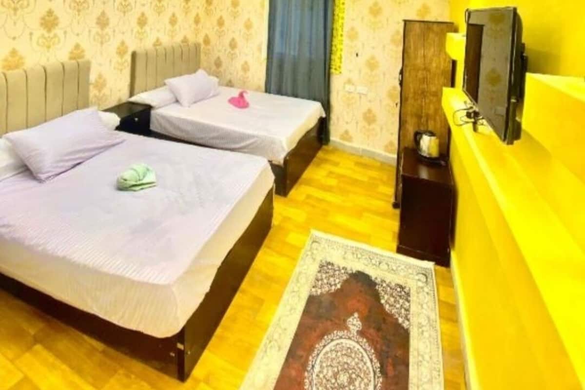 A hotel room with two beds, a TV, and a wooden floor.