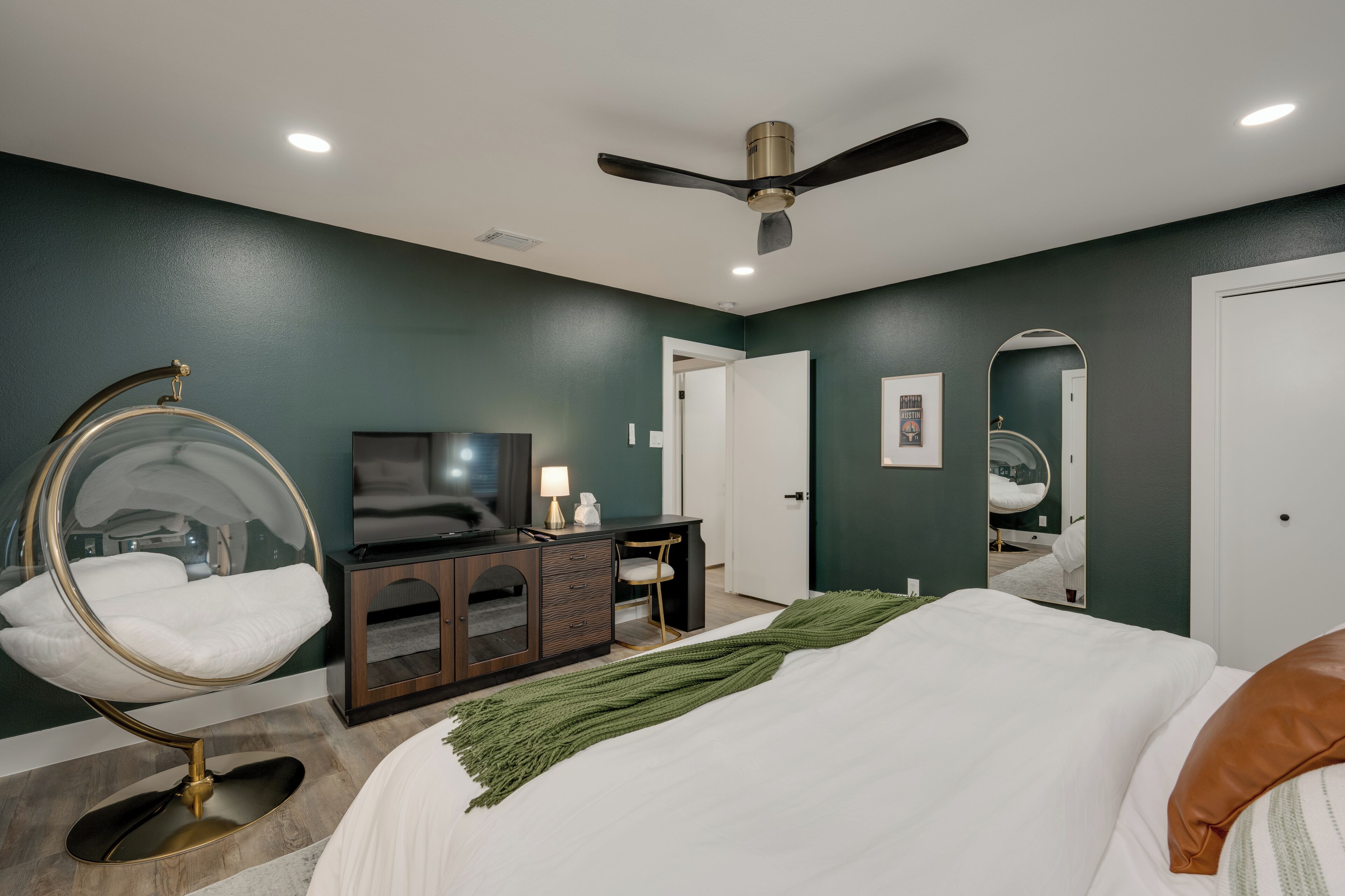 Une chambre à coucher comprenant un lit, un bureau, une chaise, un téléviseur et un ventilateur de plafond.