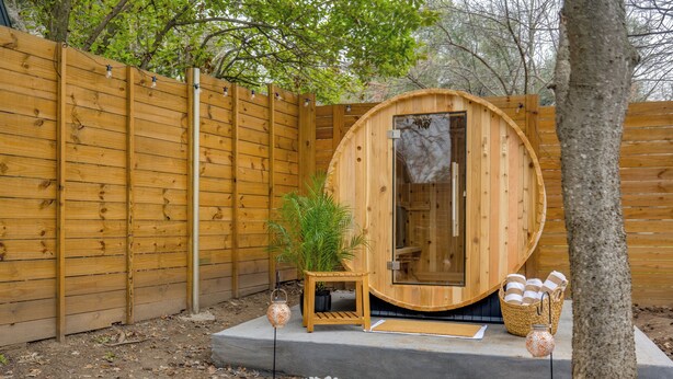 A wooden sauna with a curved roof, a small seating area with cushions, and a basket of towels. -  5-Bedroom Retreat with Cowboy Pool, Sauna and More – 10 Min to Downtown Austin (Austin)