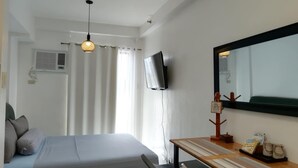 Una habitación de hotel con cama, escritorio con espejo, televisor y ventana con cortinas.