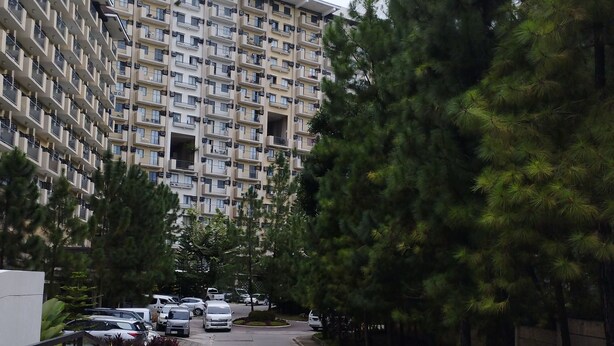 Un edificio residencial de varios pisos con balcones, un estacionamiento con coches y árboles circundantes.