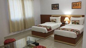 A hotel room with two beds, a glass coffee table, a small ottoman, and a window with curtains. - The Bodhgaya Hotel School (Bodh Gaya)