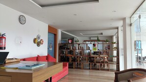 A modern living room with a wooden dining table, red sofa, and a bookshelf filled with books and decorative items. - The Bodhgaya Hotel School (Bodh Gaya)