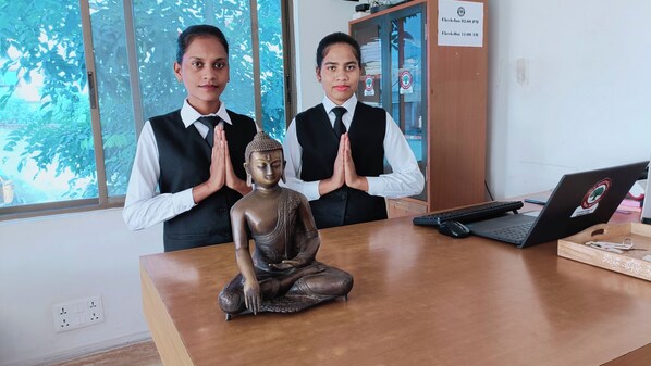 Dos personas en una habitación con una computadora portátil, una estatua de Buda y un letrero que muestra los horarios de registro de entrada y salida.