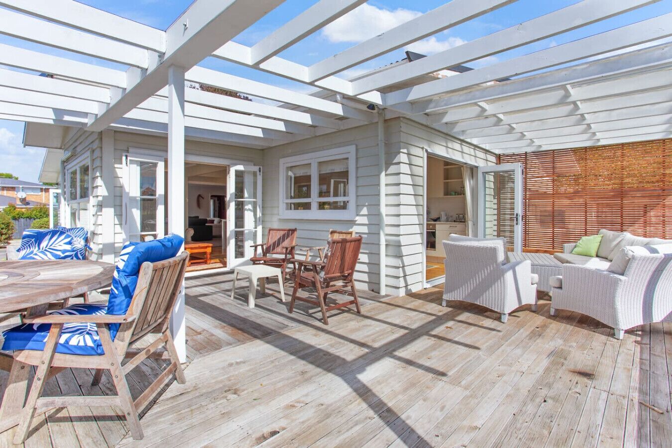Eine überdachte Terrasse im Freien mit Holzboden, weißer Möbel und einer Pergola.