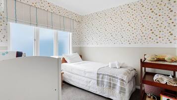 A bedroom with a single bed, a window with blinds, a wooden shelf with toys, and a polka dot wall.