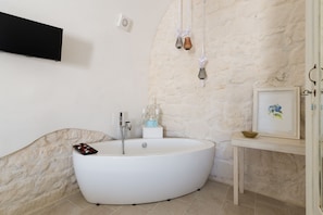 A modern bathroom with a freestanding bathtub, a small table with a framed picture, and a wall-mounted light fixture.