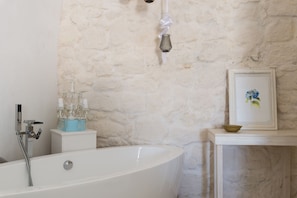 A bathroom with a freestanding bathtub, a towel rack, a framed picture on the wall, and a small shelf with a bowl.