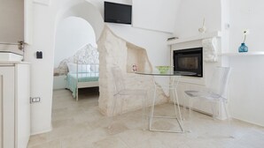 A modern, minimalist room with a bed, a TV, a fireplace, and a dining area with transparent chairs. - Petra Suite Ostuni by Wonderful Italy (Ostuni)