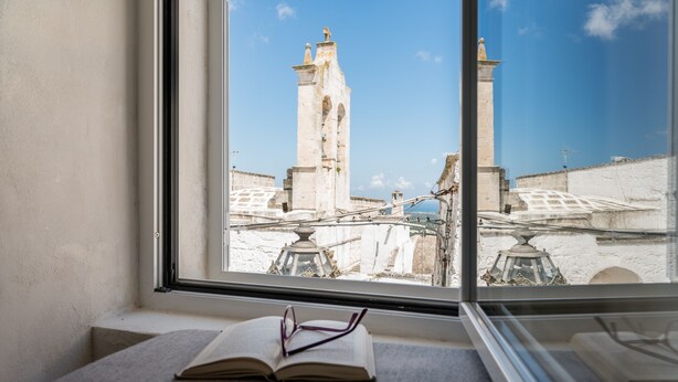 A window with an open book and glasses on a ledge, overlooking a historic stone bridge and towers. - Petra Suite Ostuni by Wonderful Italy (Ostuni)