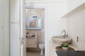 A bathroom with a white sink, a blue-framed mirror, a white toilet, and a stone basin.