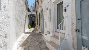 A narrow stone staircase leading to a white door with a green window, a small potted plant, and a sign with a rooster. - Petra Suite Ostuni by Wonderful Italy (Ostuni)