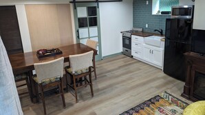 A compact kitchen with a dining area, featuring a wooden table, chairs, a stove, a refrigerator, and a microwave. - Charming studio. Close to highway and ferries. (Bremerton)
