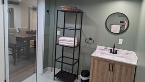 A bathroom with a wooden cabinet, a marble sink, a black shelf with towels, and a mirror. - Charming studio. Close to highway and ferries. (Bremerton)