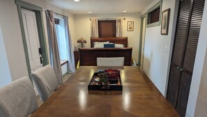 A dining room with a long wooden table, two upholstered chairs, a decorative tray with items, and a bed with a headboard in the background. - Charming studio. Close to highway and ferries. (Bremerton)