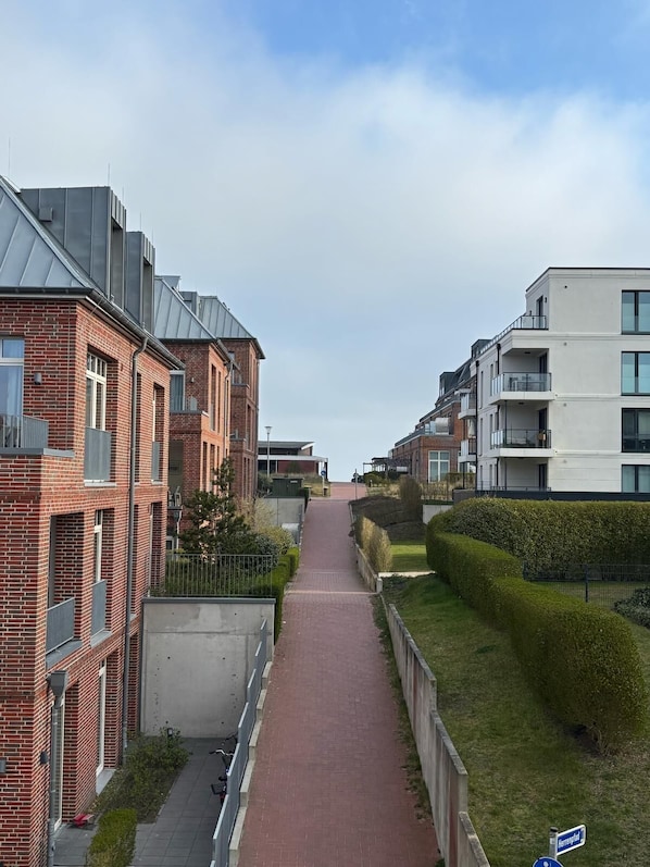 A residential street with brick houses and modern buildings, a paved walkway, and well-maintained hedges.