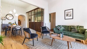 Un salon spacieux avec un canapé vert, un coin repas doté d’une table ronde et une grande fenêtre offrant une vue dégagée.