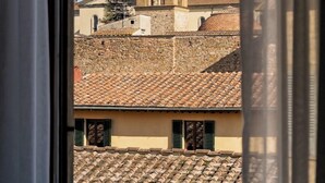 Une vue d’une tour historique, aperçue à travers une fenêtre, avec un bâtiment aux tuiles de terre cuite en premier plan.