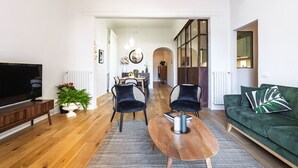 Un salon moderne avec une table basse en bois, deux chaises noires, un canapé vert et un téléviseur à écran plat.
