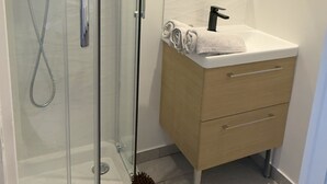 A modern bathroom with a glass shower enclosure, a wooden vanity with a mirror, and a towel on the sink.