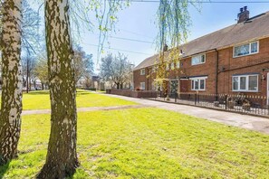 A residential street with houses, a grassy area, and trees.