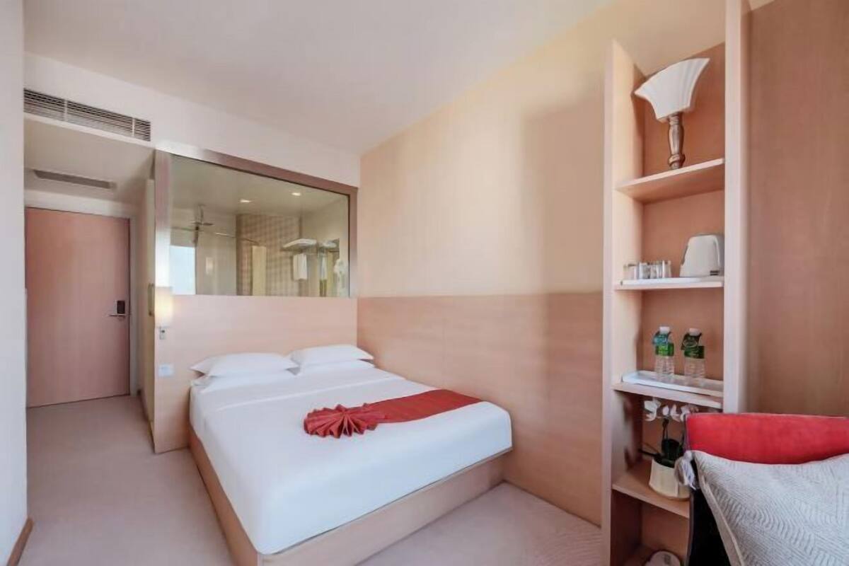 Une chambre d’hôtel avec un lit, un miroir, une étagère avec des articles de toilette et une serviette rouge.