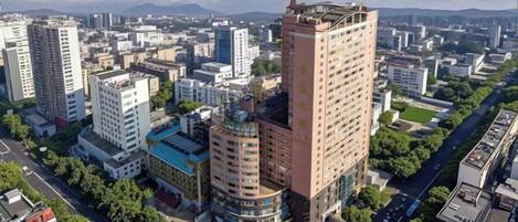 A high-rise building with a rooftop garden, surrounded by other buildings and a clear sky.