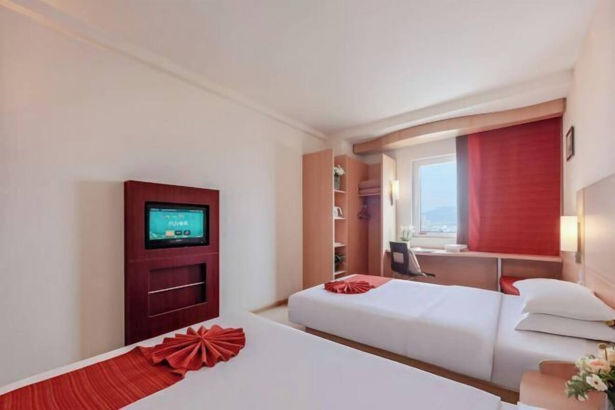 Une chambre d’hôtel avec deux lits, une télévision, un bureau et une fenêtre avec un rideau rouge.