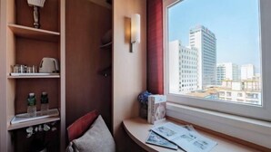 A hotel room with a large window, a desk with a lamp, a bookshelf, and a view of city buildings. - Longma Ginza Hotel (Yuxi)