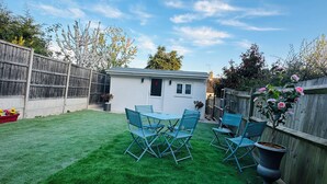 A backyard with artificial green grass, a small shed, and a wooden fence. - Cosy and Comfy Double Room with Private Bathroom, Close to o2 Arena (London)