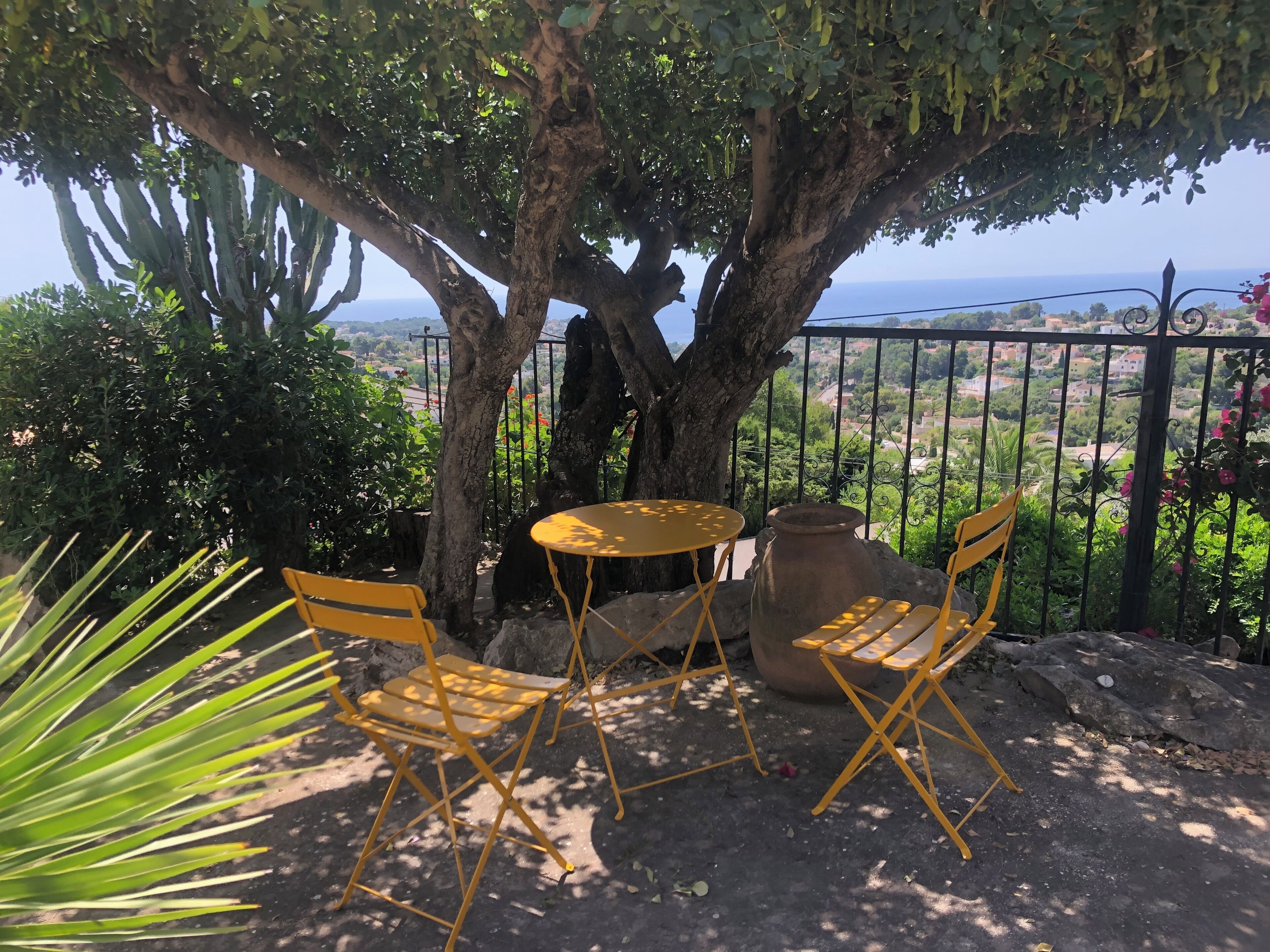 Une terrasse avec des chaises pliantes jaunes, une table ronde et un grand pot de fleurs.