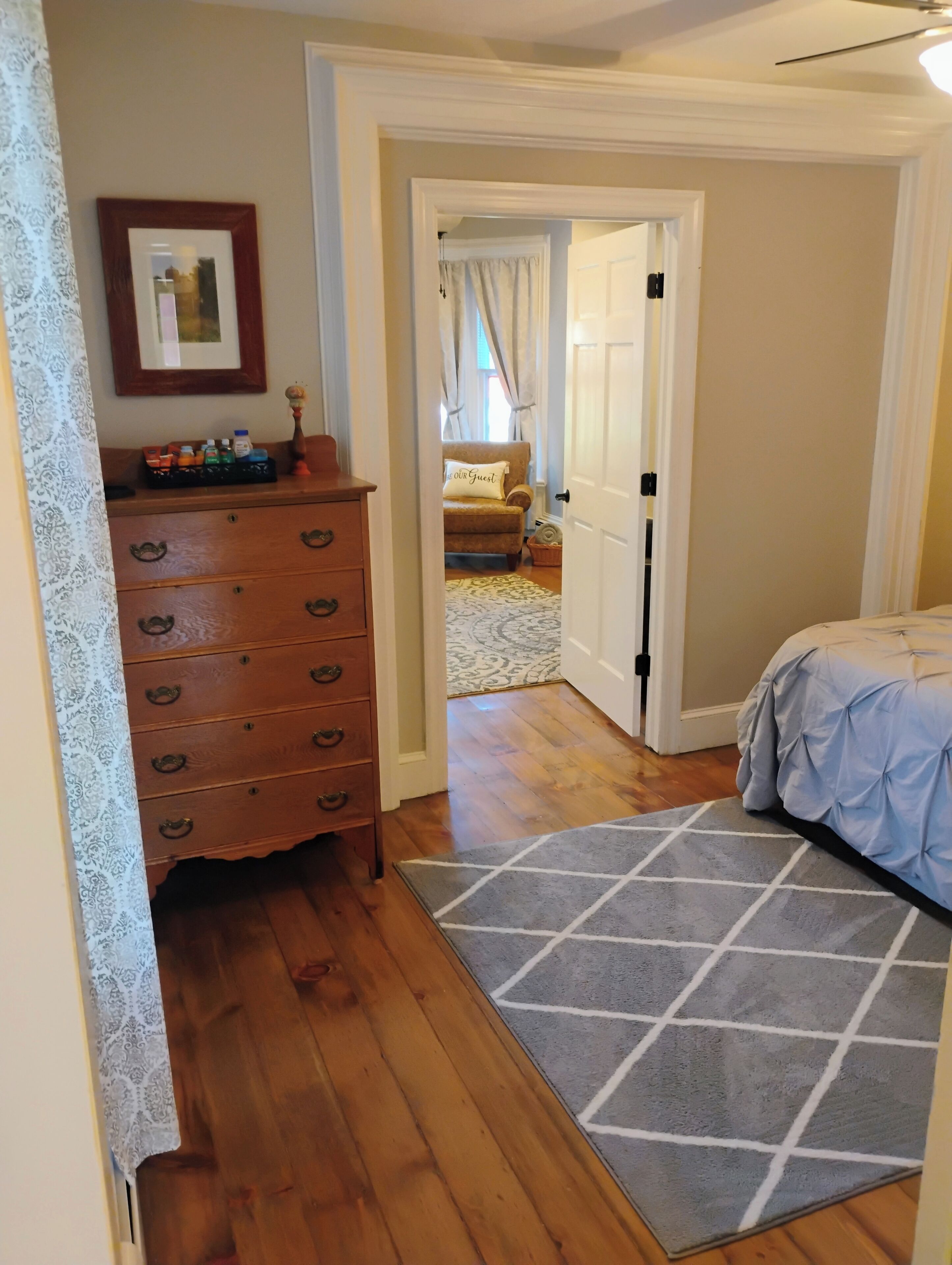 Un dormitorio con un aparador de madera, una cama con cubrecama azul y una alfombra estampada.